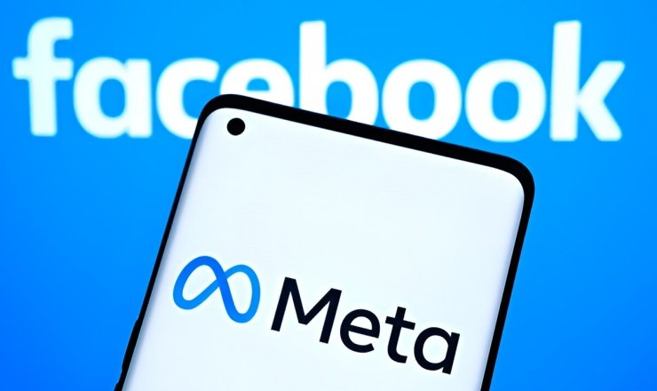 Smartphone mostrando el logo de Meta frente a una computadora